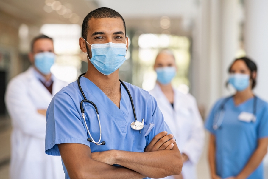 Healthcare worker with mask smiling with other healthcare workers in the background