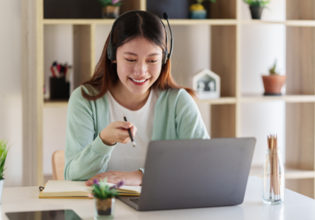 A student in an online class with a headset on sits in front of a laptop and holds a pencil.