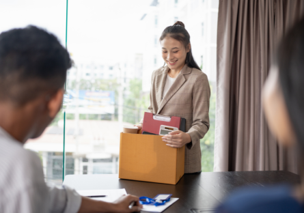 A woman hands in her resignation to her superiors as she prepares to leave with a box of her things.