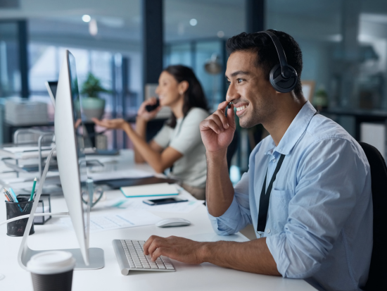 An IT worker sits in front of his computer, smiling and talking to a customer over his headset.