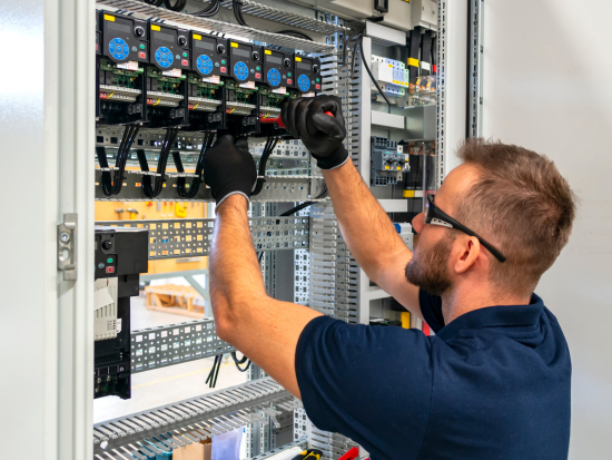 Electrical technician installing and wiring components inside an industrial control panel.