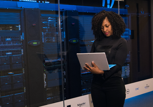 Female professional standing with a laptop next to data centers. 