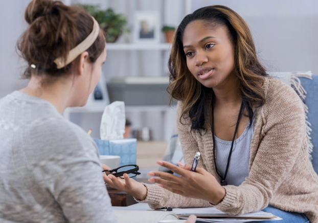 Female behavior technician speaking with a female patient in an office setting.