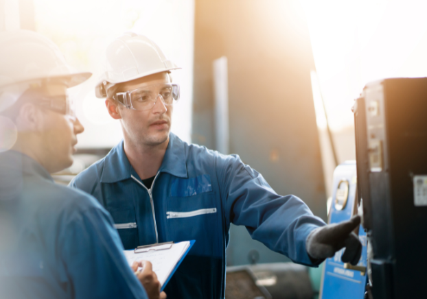 Two male engineering technicians with hard hats looking at piece of industrial equipment